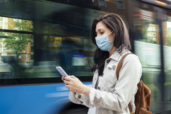Woman standing in the bus stop. She is wearing a protective mask for the prevention of a virus. Coronavirus concept.