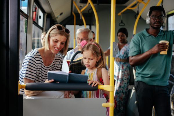 A young adult mom and her daughter are reading a book while they're riding a city bus