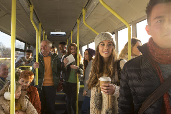 Different people can be seen travelling on the bus. Some are talking to other people, others are using technology or looking out the window.