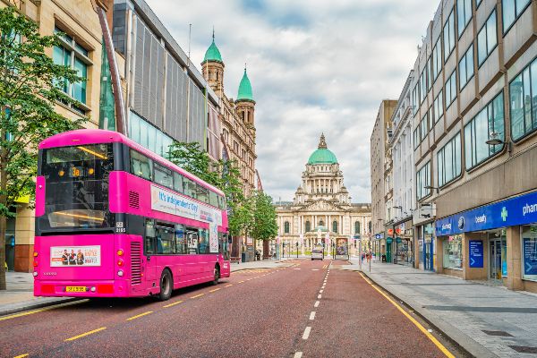 Bus stands at a bus stop with The City Hall building in the background in downtown Belfast Northern Ireland on a cloudy day. Public Transport Statistics Northern Ireland 2022-23